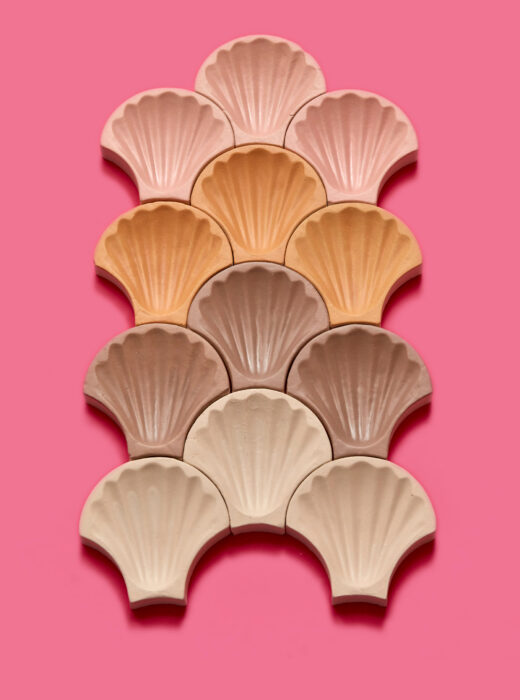 Piastrelle a forma di conchiglia in varie tonalità di rosa e marrone su sfondo rosa.