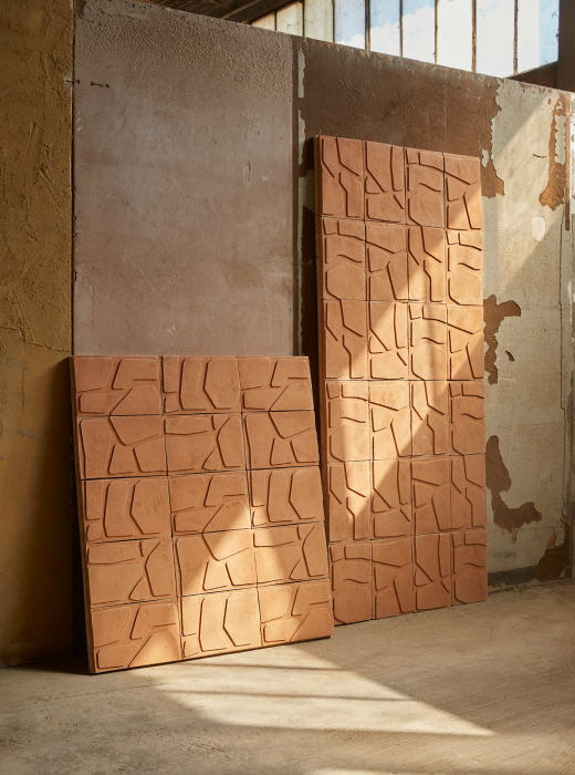 Pannelli in terracotta con motivo geometrico appoggiati a una parete in un ambiente industriale
