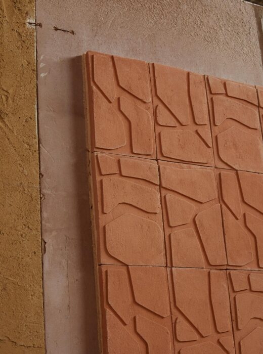 Rivestimento murale in terracotta con piastrelle quadrate con motivo geometrico a rilievo.