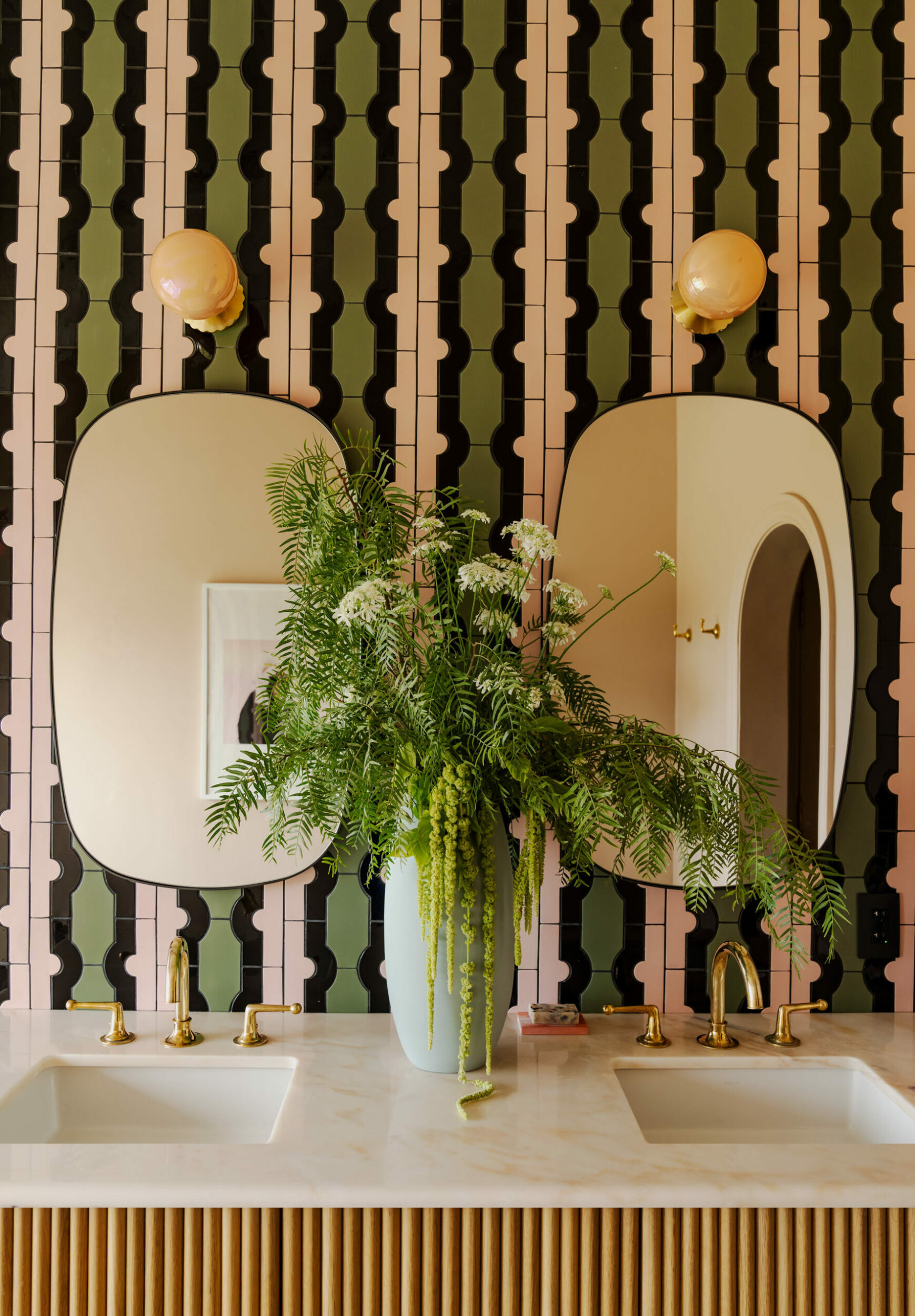 Bagno con due lavabi, specchi ovali e una parete rivestita con piastrelle verdi e rosa.