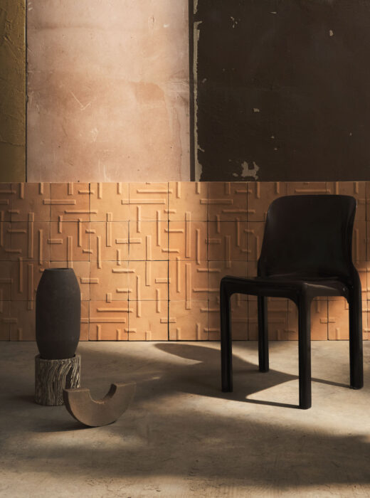 Una sedia nera davanti ad una parete rivestita con piastrelle in terracotta con motivo geometrico, in un ambiente industriale