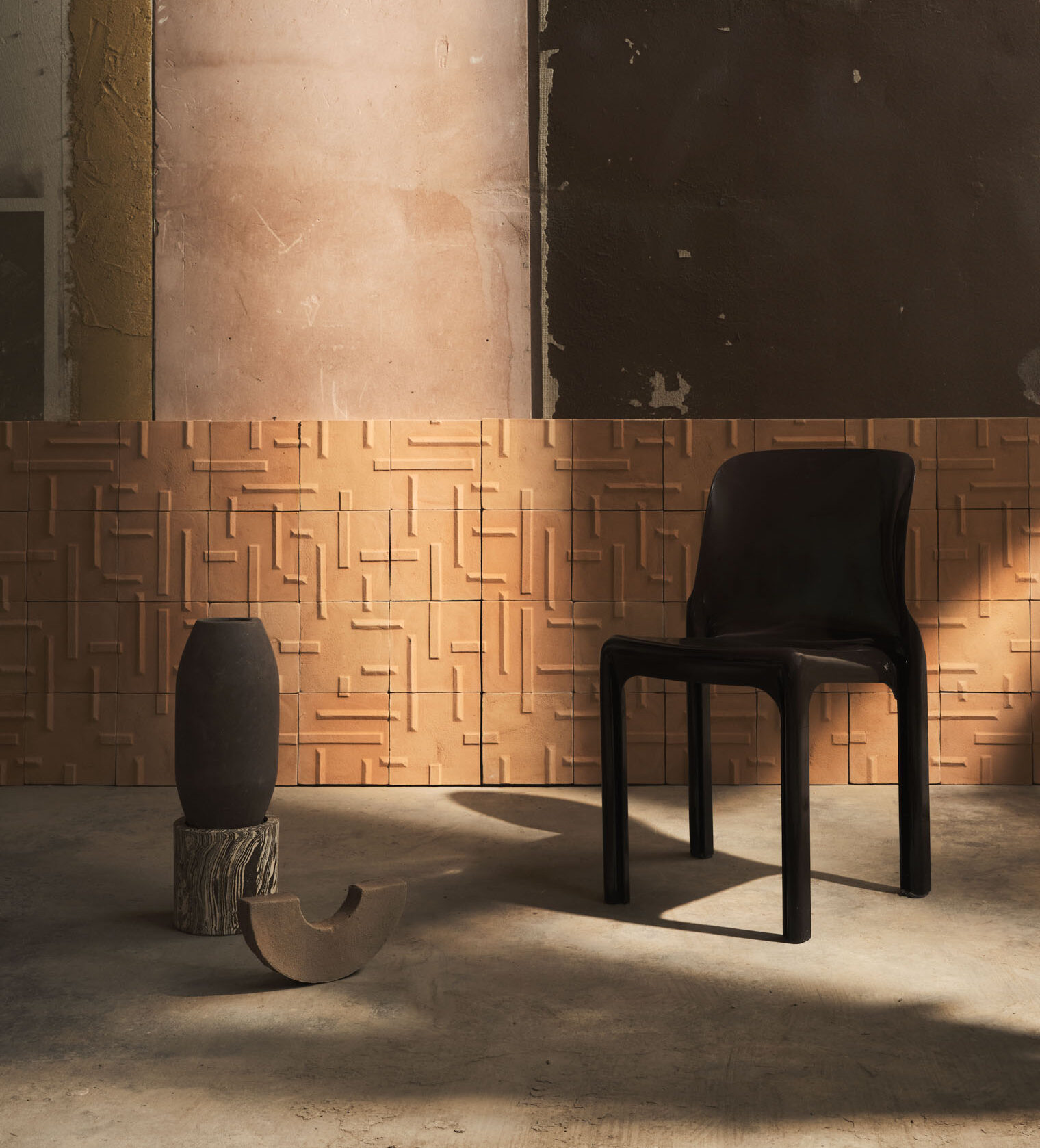 Una sedia nera davanti ad una parete rivestita con piastrelle in terracotta con motivo geometrico, in un ambiente industriale