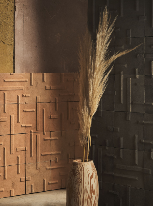 Parete rivestita con piastrelle in terracotta con motivo geometrico, vaso di ceramica con piume di pampas.