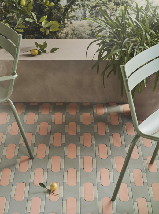 Pavimento con piastrelle rosa e verdi, sedie verdi e piante decorative con limoni sullo sfondo