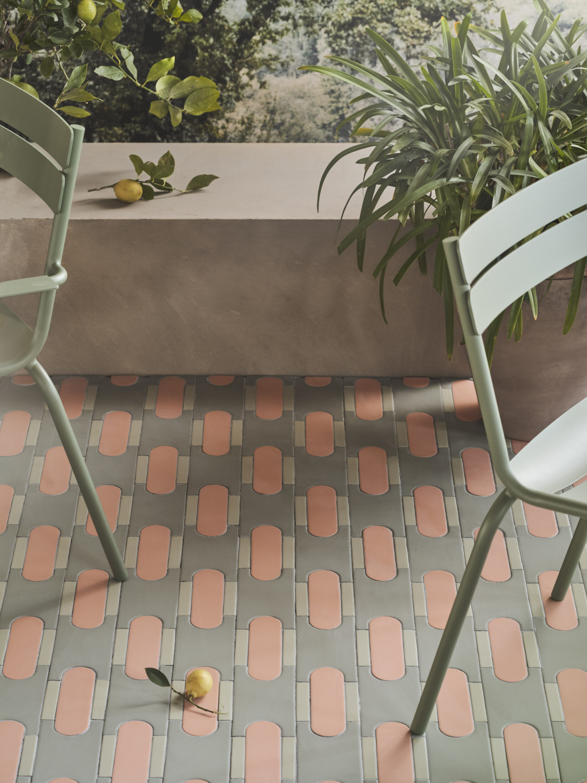 Pavimento con piastrelle rosa e verdi, sedie verdi e piante decorative con limoni sullo sfondo