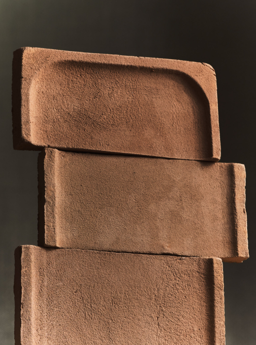 Elementi modulari in terracotta con texture ruvida e forme geometriche sovrapposte su sfondo scuro