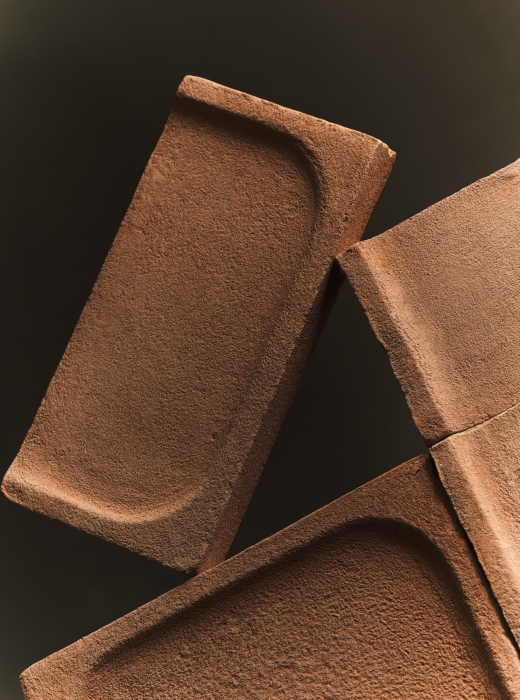 Moduli in terracotta con superfici concave e texture ruvida, disposti in composizione geometrica su sfondo scuro
