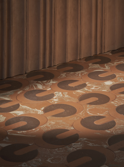 Pavimento in terracotta con motivi circolari e parete ondulata sullo sfondo