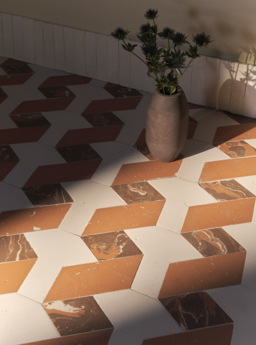Pavimento geometrico in terracotta e marmo con vaso scuro contenente fiori spinosi