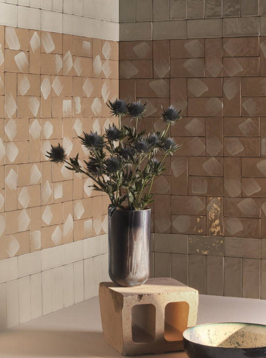 Parete in piastrelle decorate con vaso metallico contenente fiori spinosi su un blocco di terracotta, con una ciotola decorativa in primo piano
