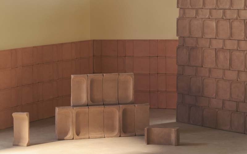 Moduli in terracotta impilati in una stanza con pareti rivestite dello stesso materiale e giochi di luce naturale.