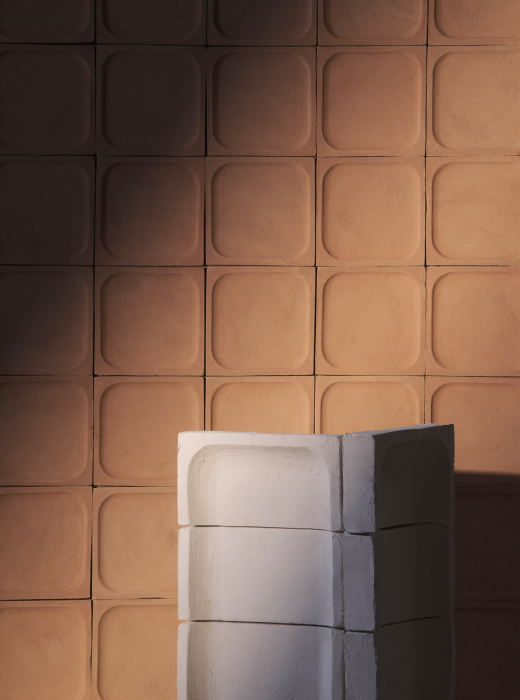 Parete in terracotta con moduli concavi e struttura in ceramica bianca in primo piano, illuminata da luce naturale
