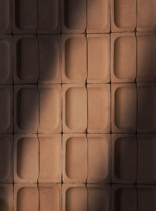 Sedia con seduta gialla su pavimento in terracotta a motivi geometrici, illuminata dalla luce naturale