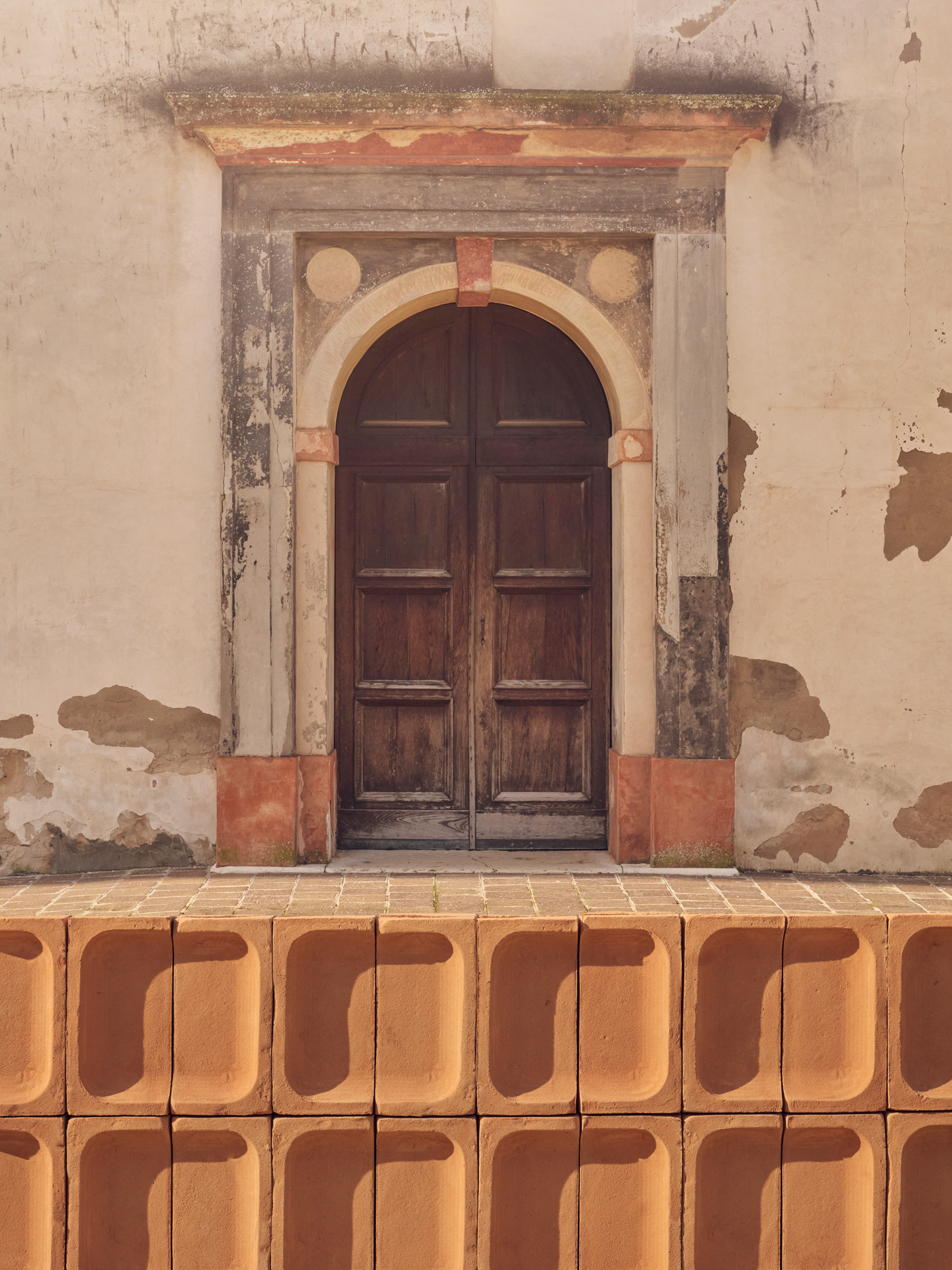 Porta in legno ad arco su una parete scrostata, con blocchi di terracotta decorativi in primo piano